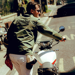 Joe wheeling his Royal Enfield while wearing our BSMC Company Coach Jacket - Khaki Green