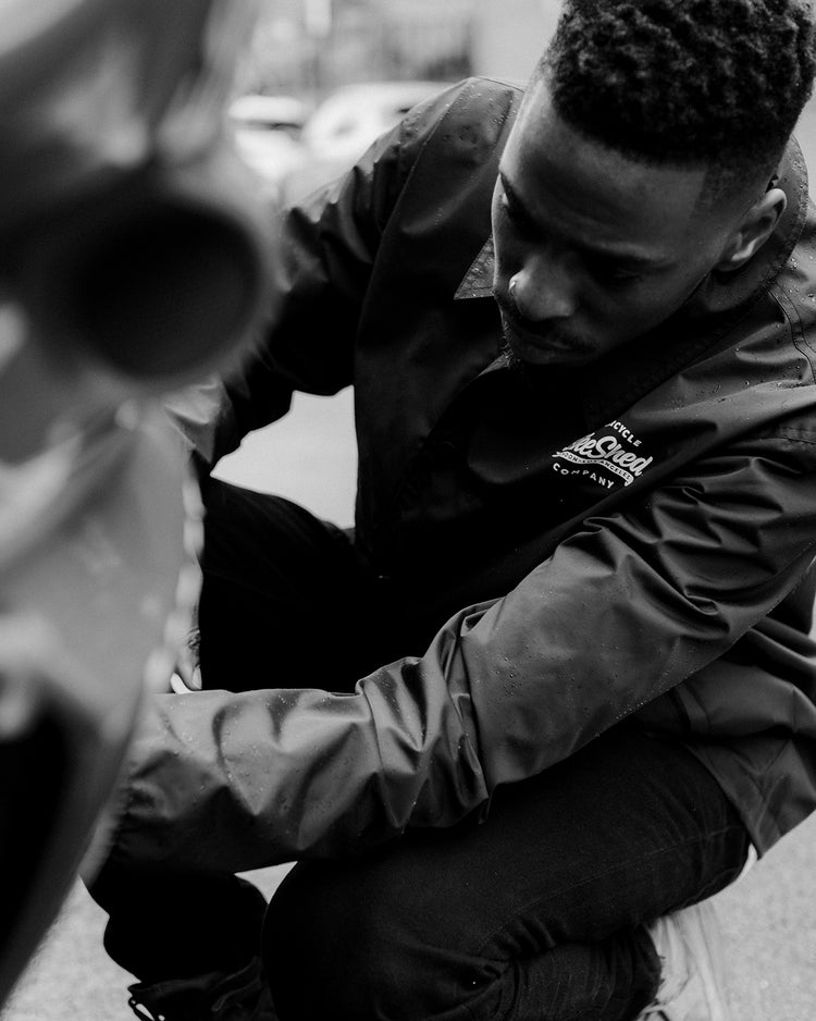 Model inspecting his bike wearing BSMC Company Coach Jacket - Black